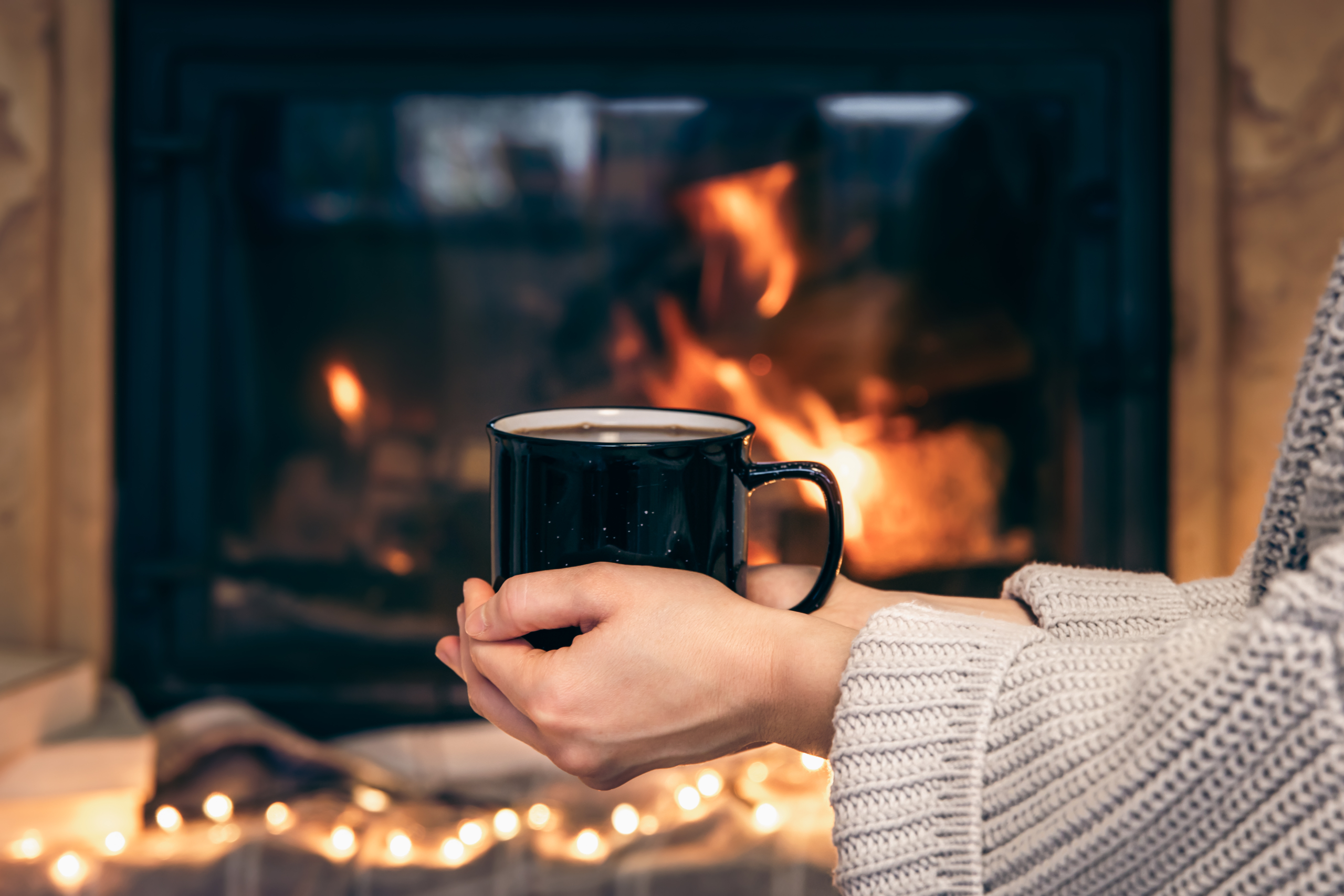 Someone holding a cup with a gas fireplace in the background.